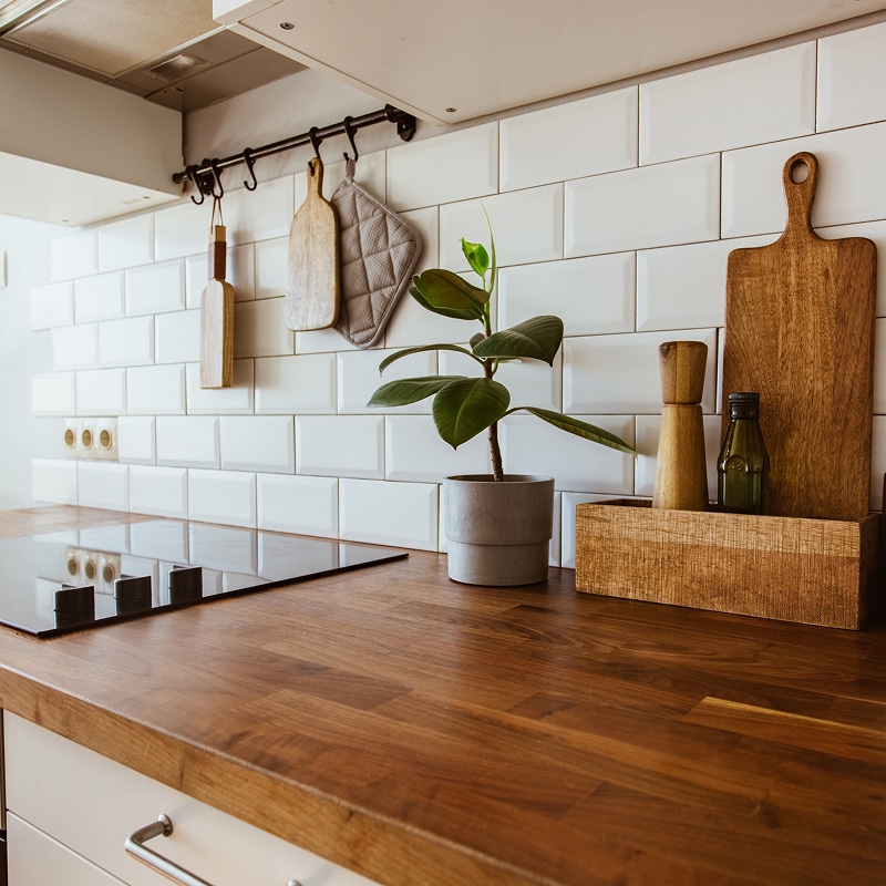 Cuisine moderne avec plan de travail en bois massif, carrelage blanc métro. Plaque induction, plante verte et ustensiles suspendus.