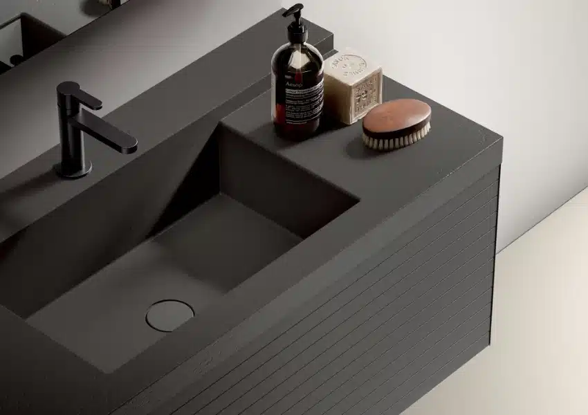 Lavabo double moderne gris foncé en pierre avec robinet noir mat. Savon Aesop et Savon de Marseille, brosse en bois sur le comptoir texturé.